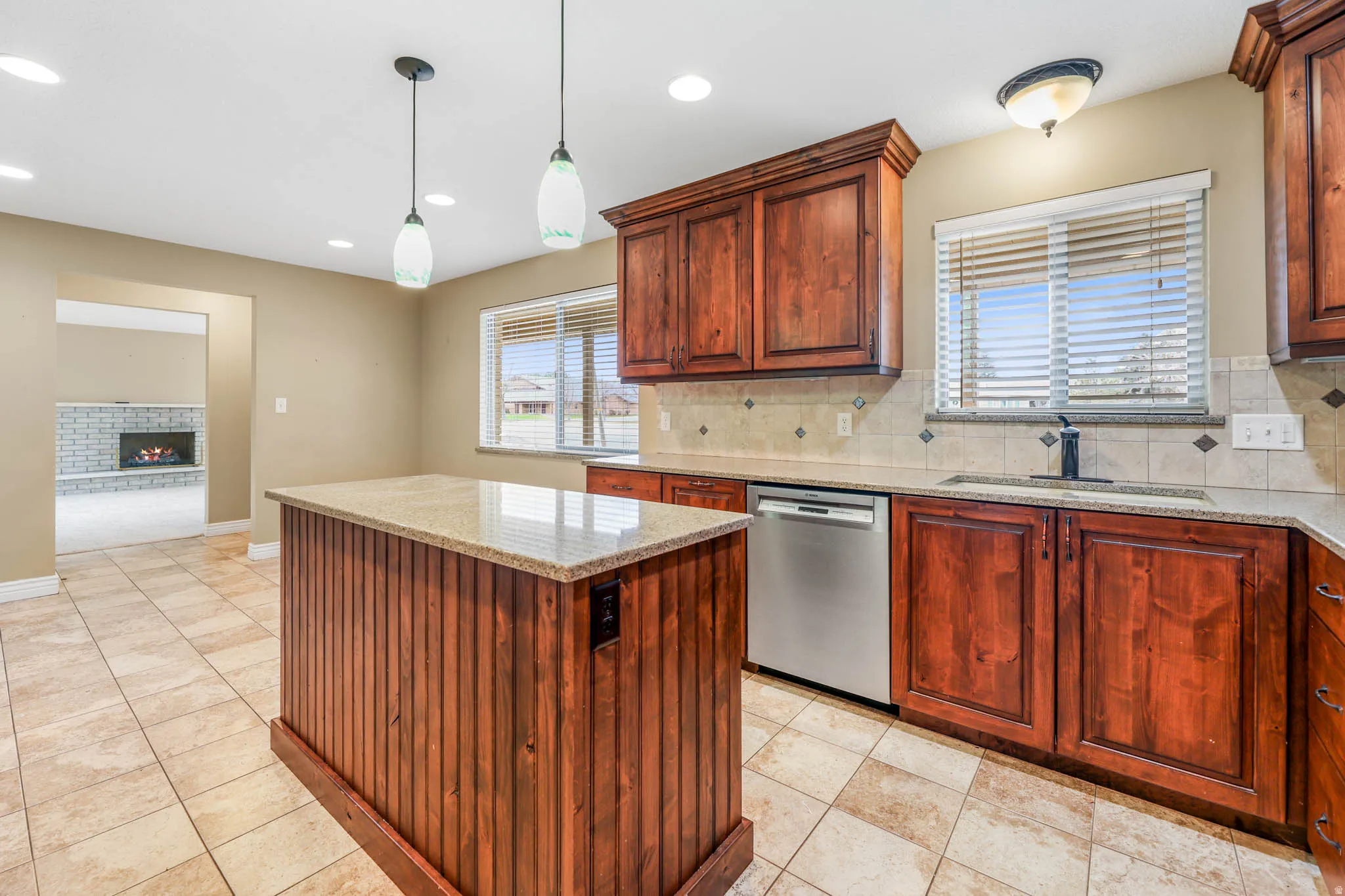 Kitchen featuring a kitchen island, tasteful backsplash, stainless steel dishwasher, light stone counters, and a fireplace