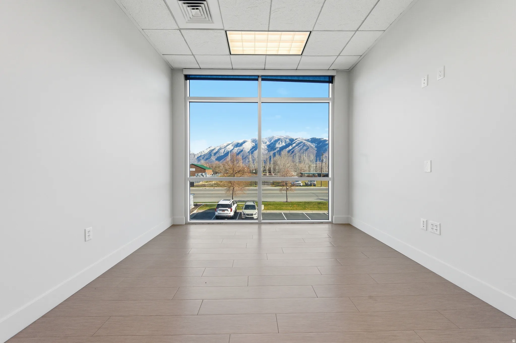 Empty room with a wall of windows, a mountain view, a paneled ceiling, and wood finished floors