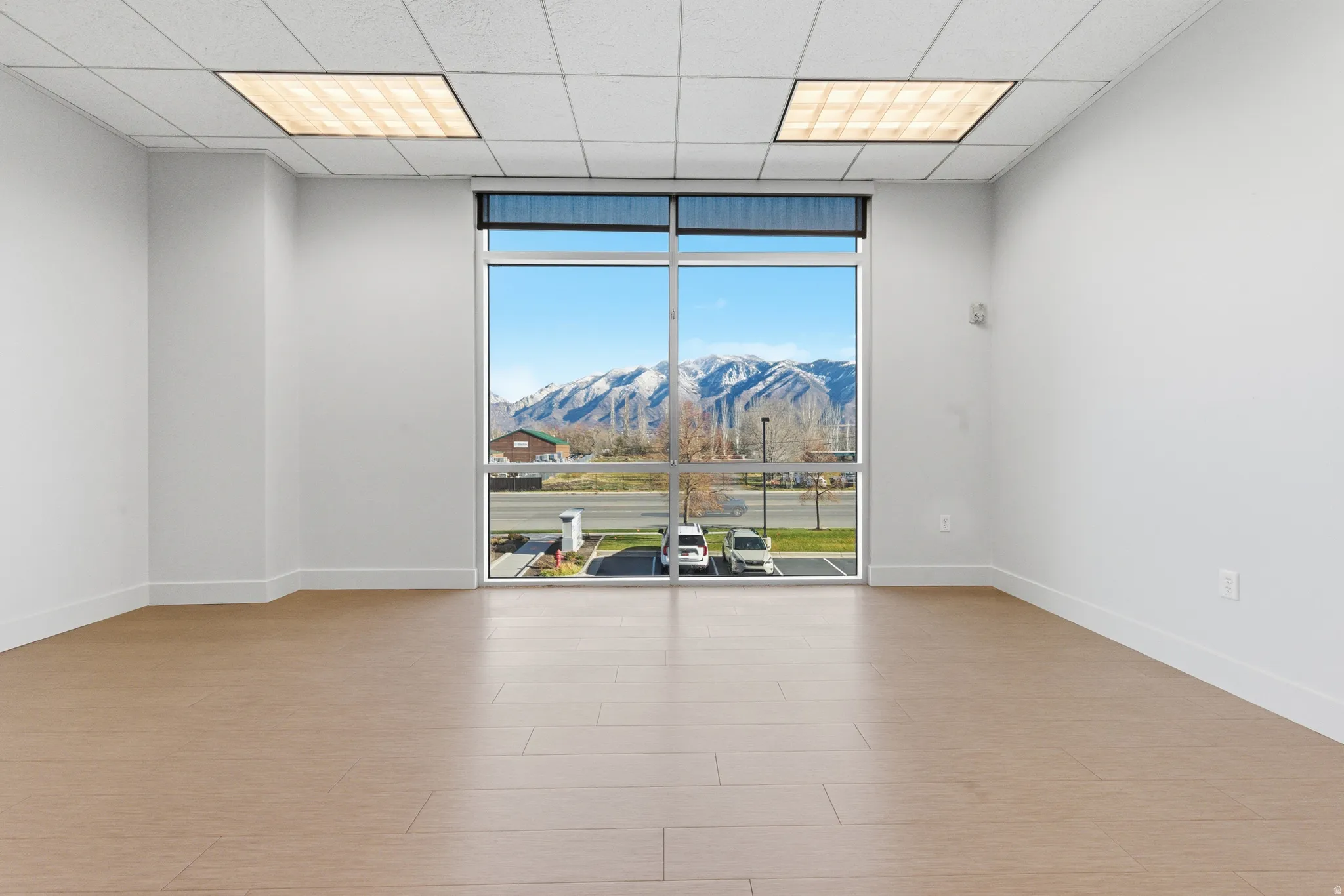 Empty room with a wall of windows, a mountain view, a drop ceiling, and light wood-style flooring