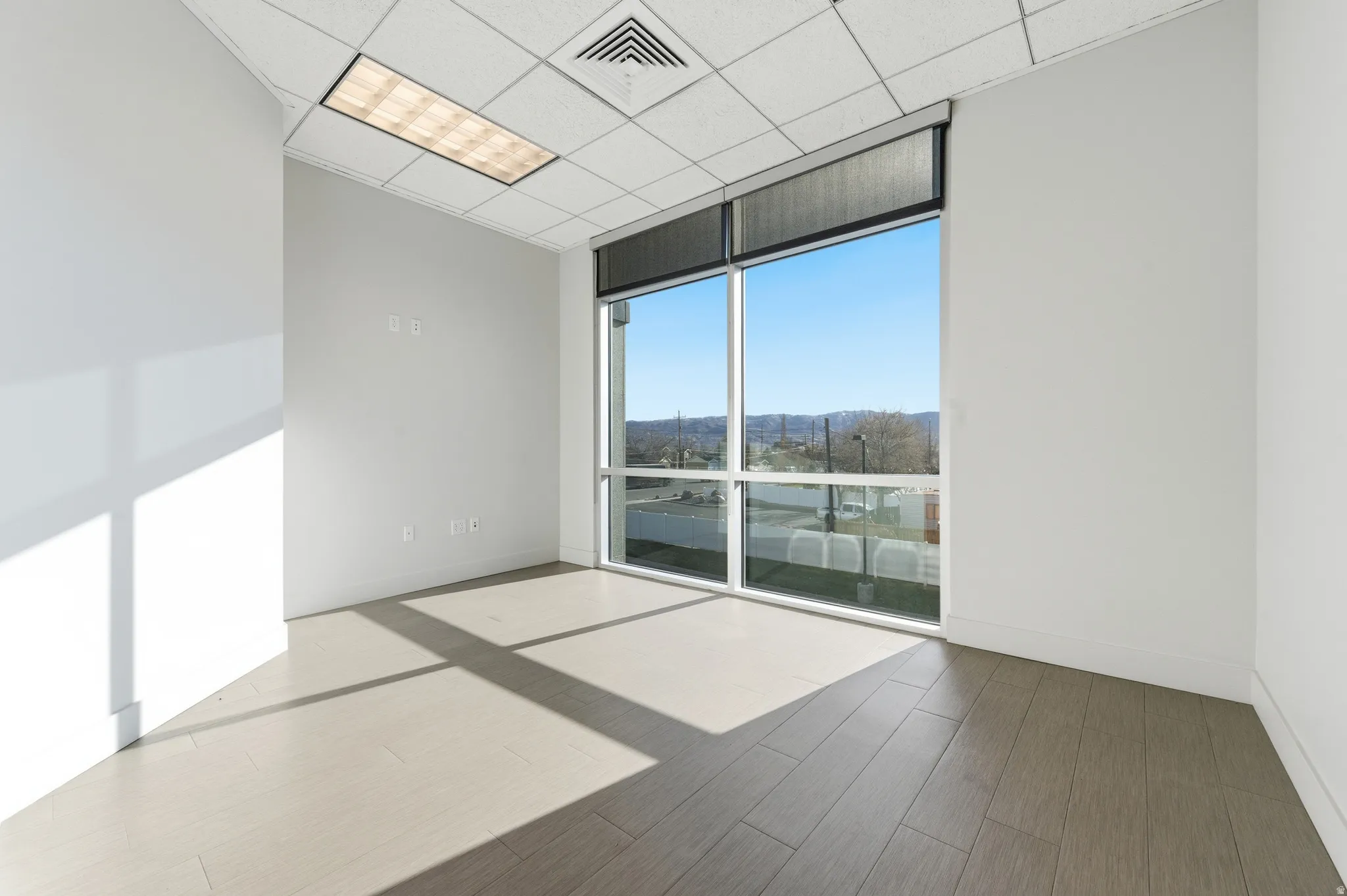 Empty room with floor to ceiling windows, wood finished floors, and a paneled ceiling