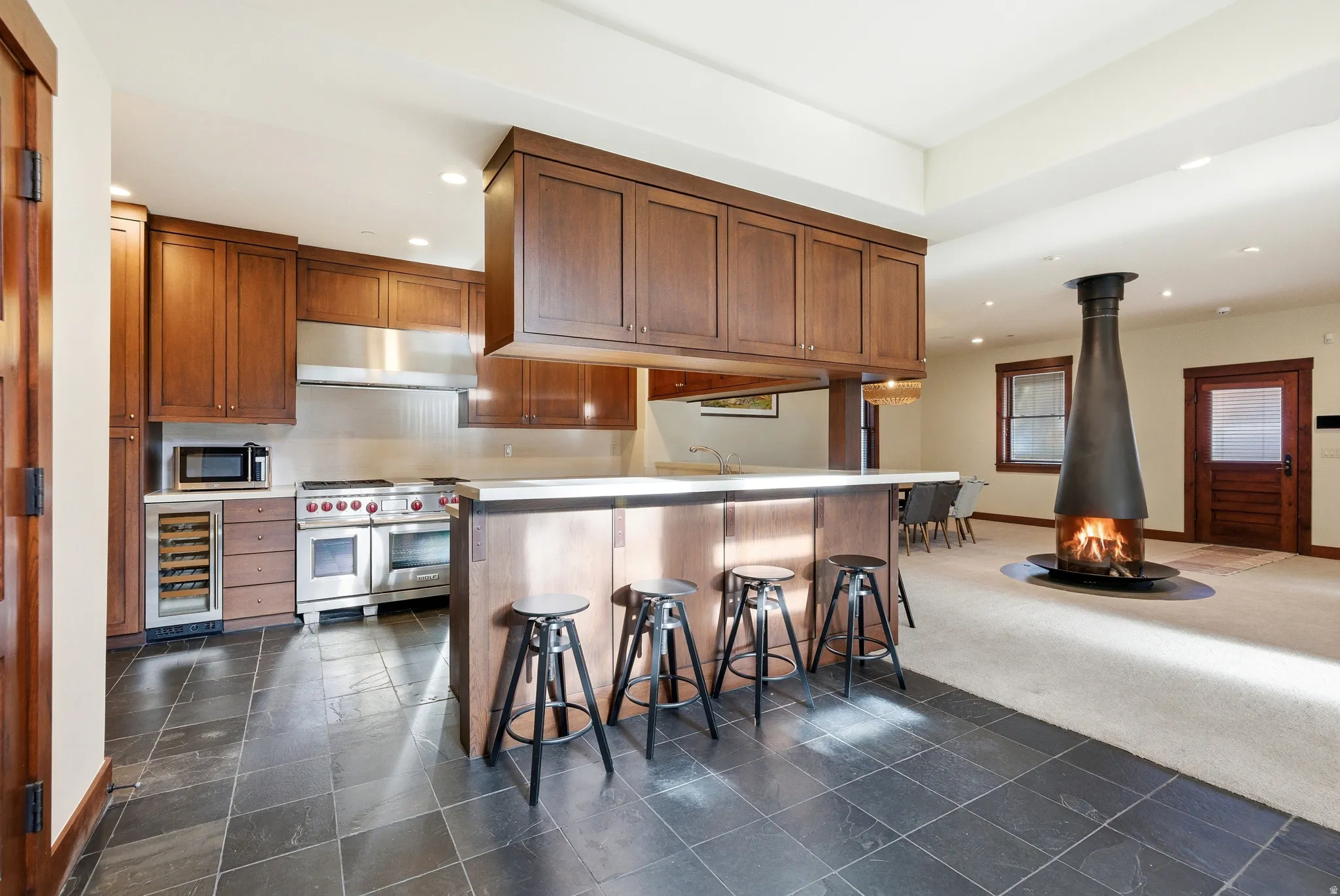 Kitchen with a breakfast bar area, dark carpet, beverage cooler, a wood stove, and stainless steel appliances