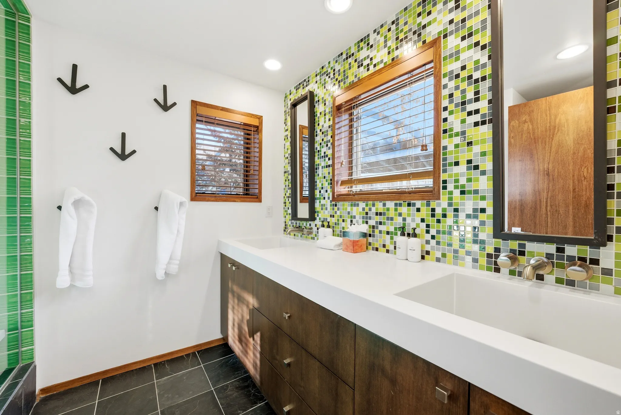 Full bathroom with double vanity, dark tile patterned floors, and backsplash