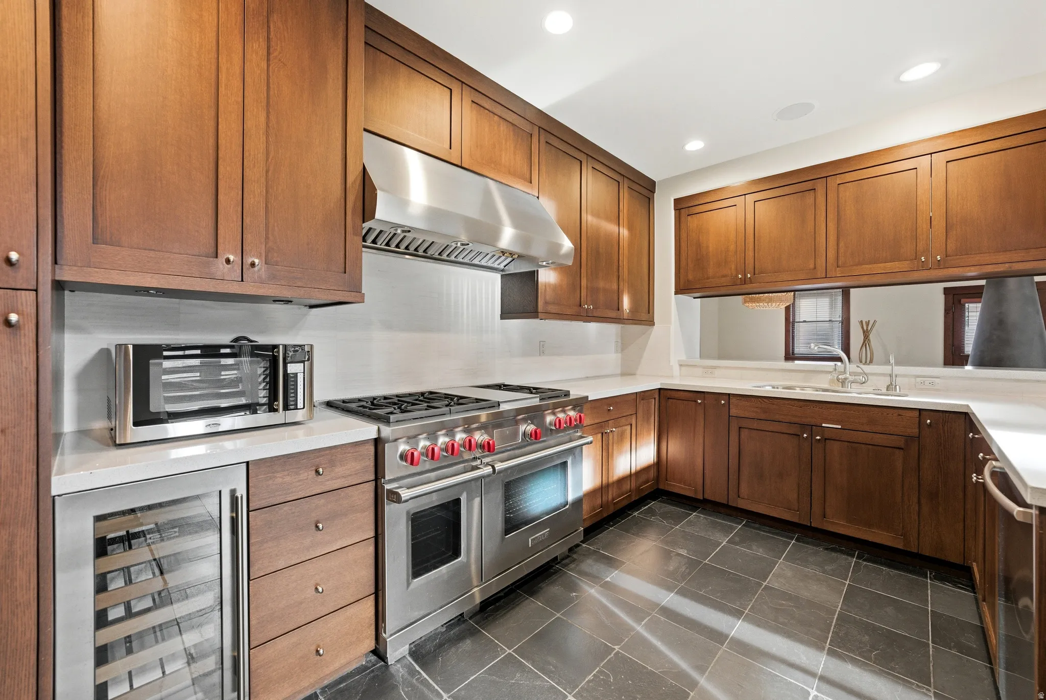 Kitchen with beverage cooler, stainless steel appliances, dark tile patterned floors, recessed lighting, and wood finish cabinetry