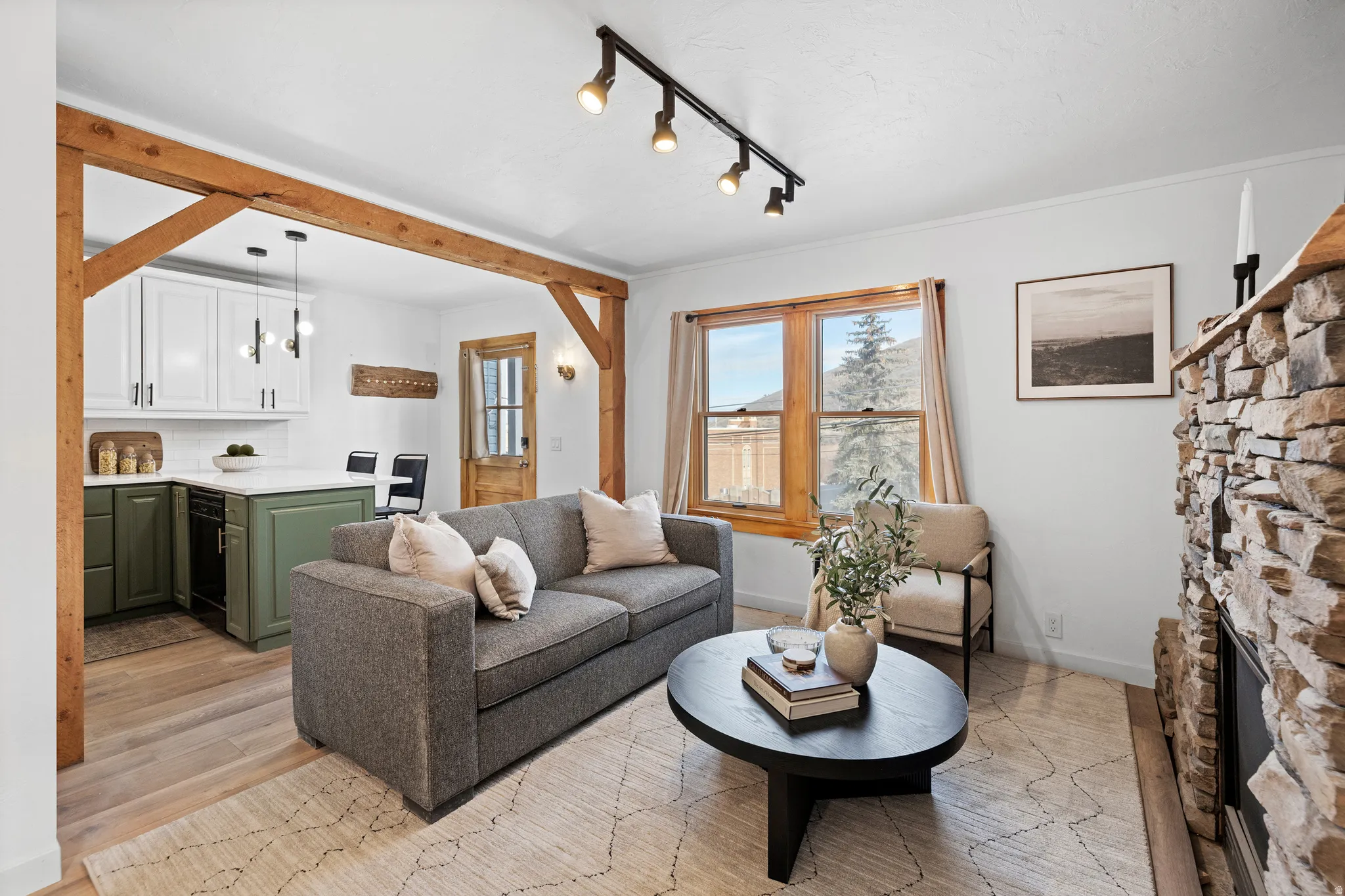 Living area with a stone fireplace, rail lighting, and light wood-style flooring