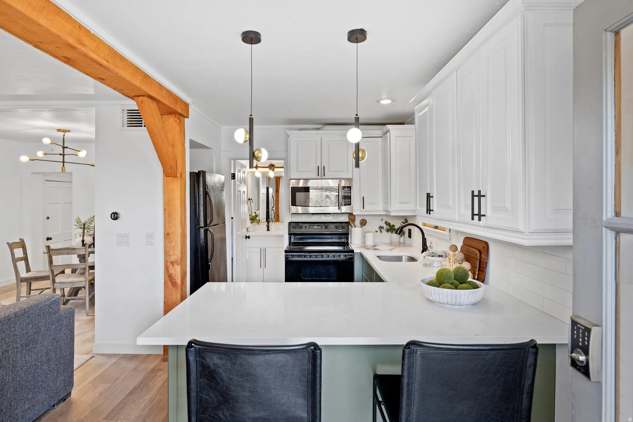 Kitchen featuring white cabinets, black appliances, a chandelier, decorative light fixtures, and light stone countertops