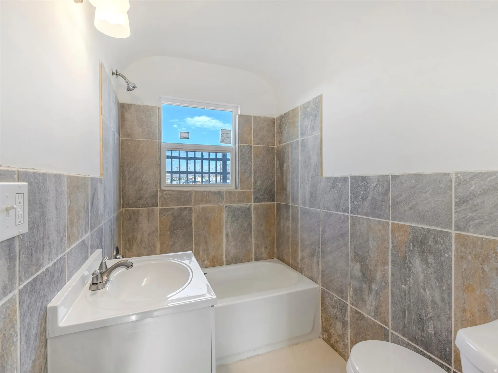 Full bathroom featuring tile walls, vanity, washtub / shower combination, and wainscoting