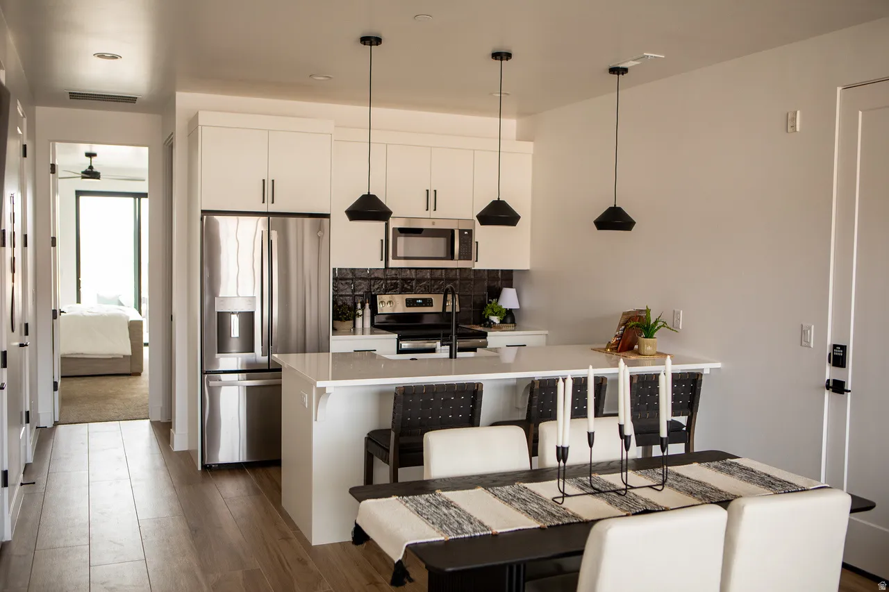 Kitchen with a peninsula, stainless steel appliances, a breakfast bar, decorative light fixtures, and white cabinetry