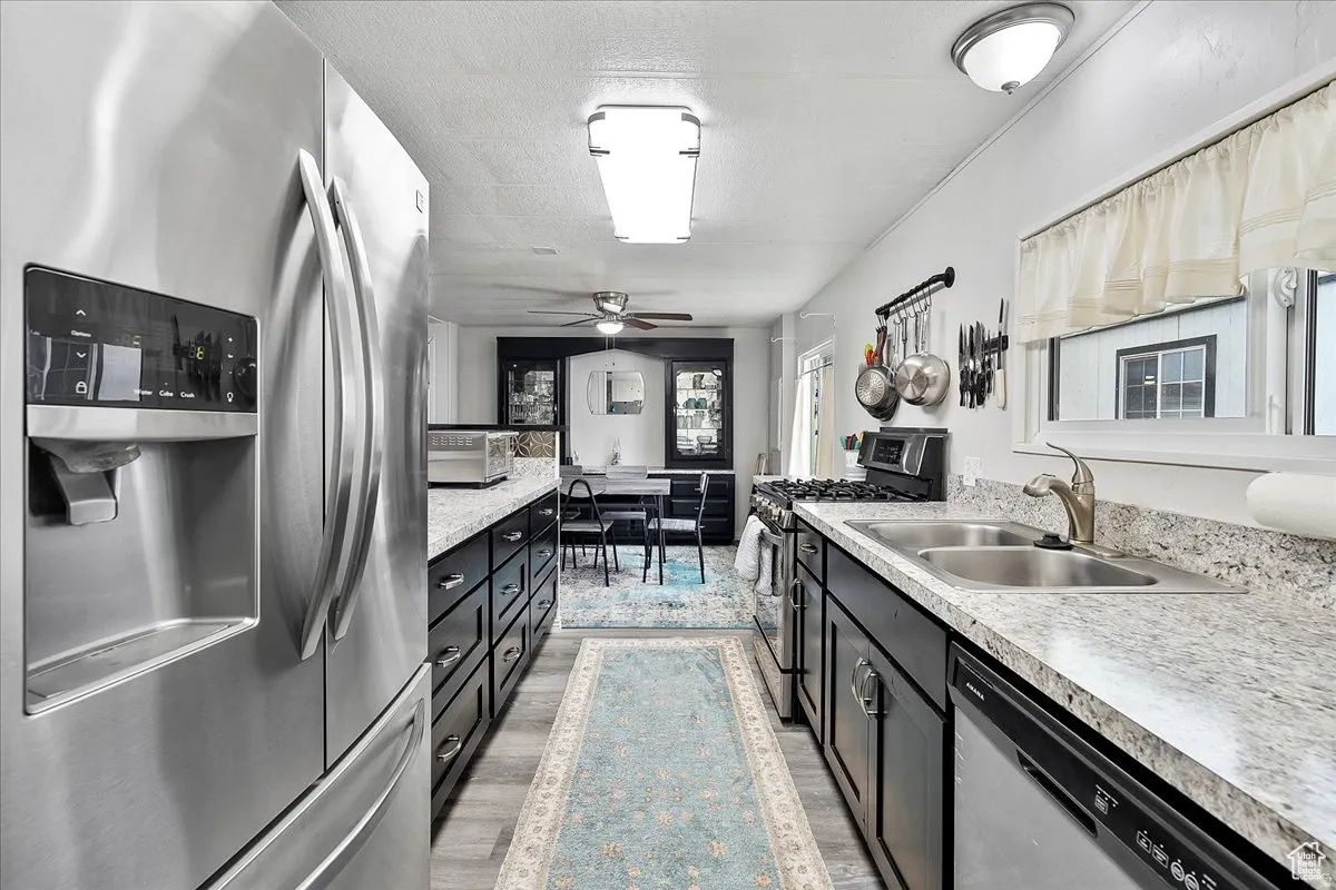 Kitchen with newer appliances with stainless steel finishes, dark cabinetry, light countertops, a textured ceiling, and light wood finished floors