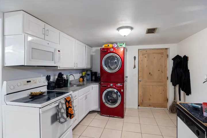 Kitchen with white appliances, white cabinetry, light tile patterned flooring, and stacked washer / dryer