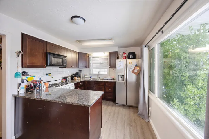 Kitchen with dark brown cabinets, stainless steel fridge, dark stone countertops, backsplash, and a peninsula
