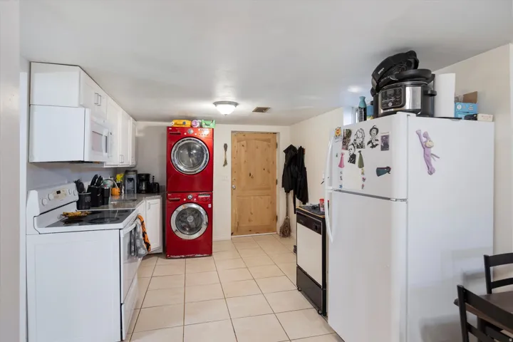 Kitchen featuring white appliances, white cabinets, light tile patterned floors, light countertops, and stacked washer / drying machine