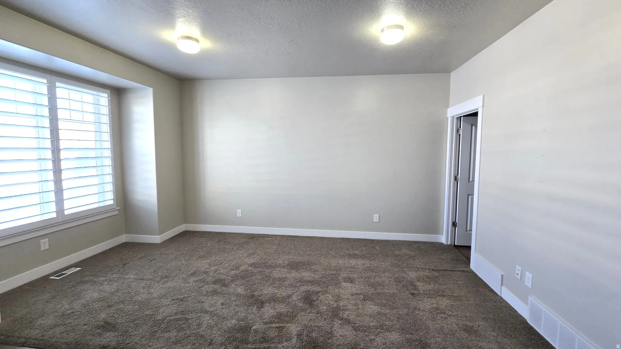 Carpeted empty room featuring a textured ceiling and baseboards
