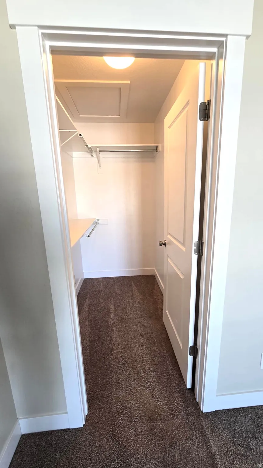 Walk in closet with dark colored carpet and attic access