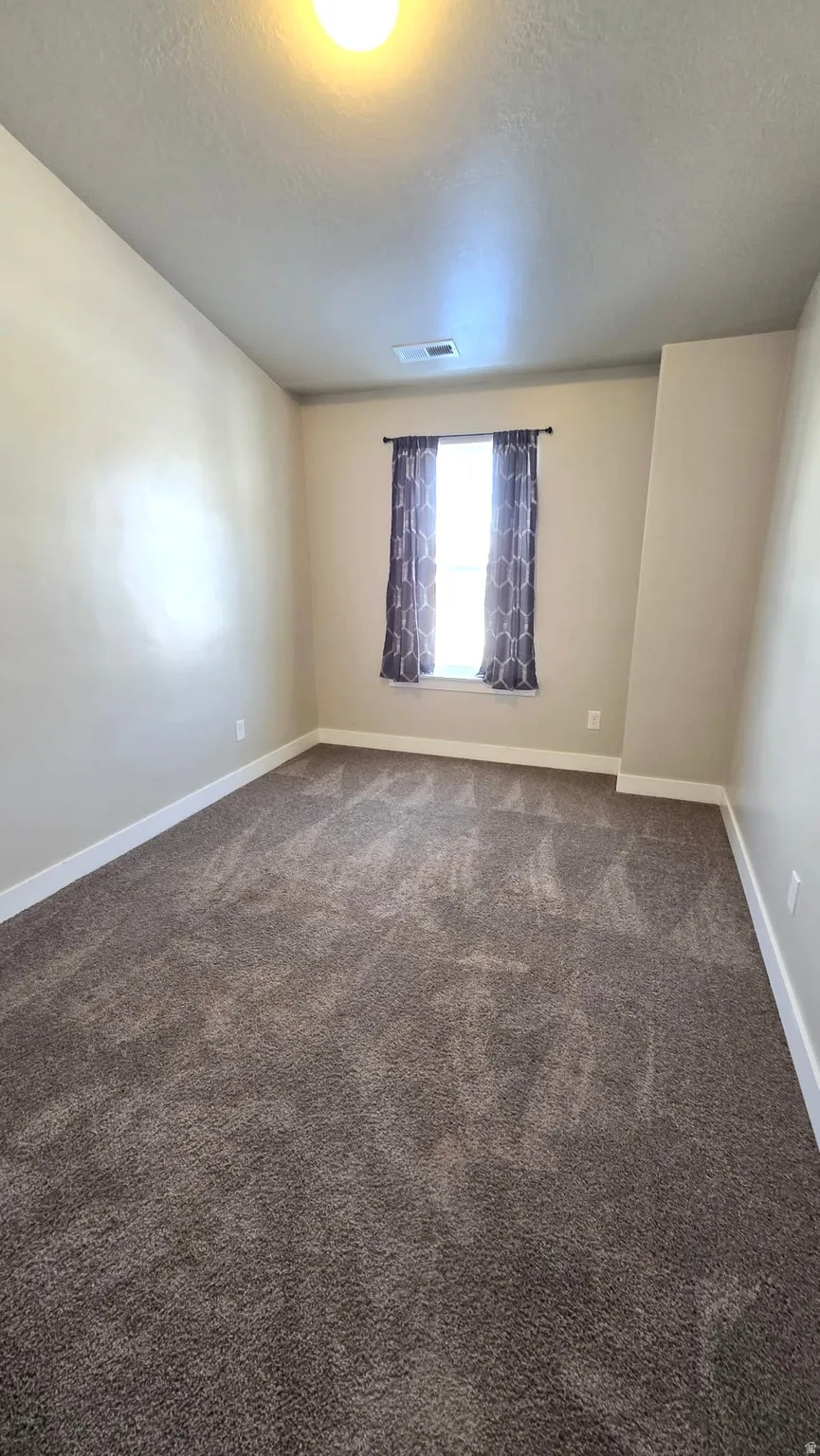 Unfurnished room featuring a textured ceiling and dark colored carpet