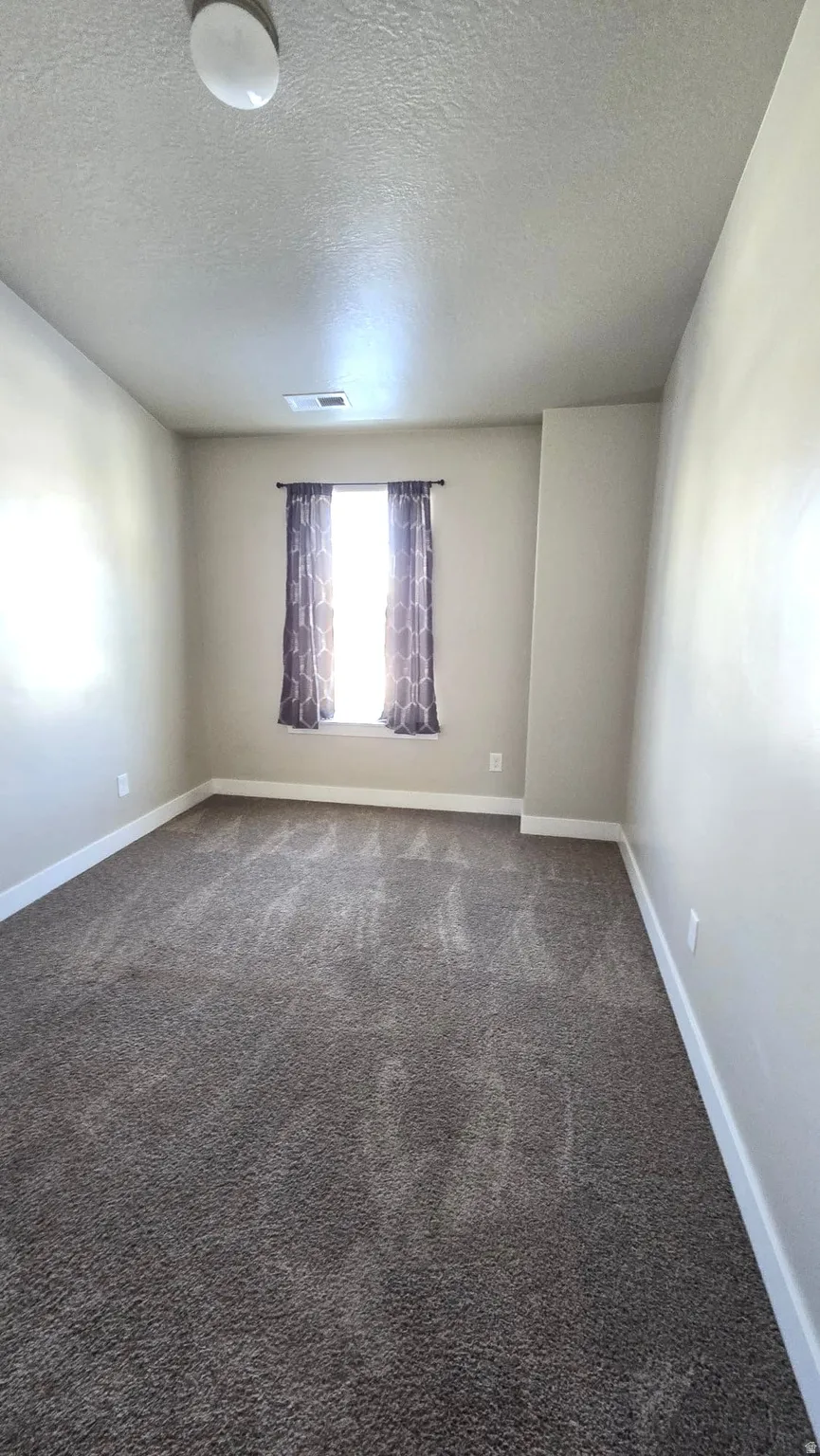 Empty room with a textured ceiling and dark carpet