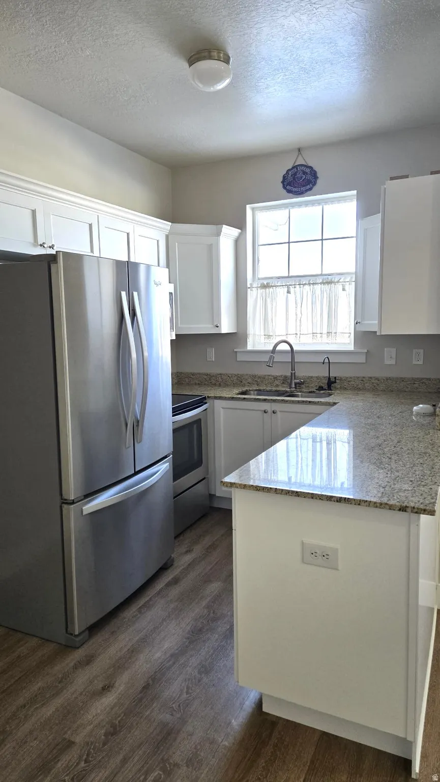 Kitchen with appliances with stainless steel finishes, a peninsula, a textured ceiling, white cabinetry, and light stone countertops