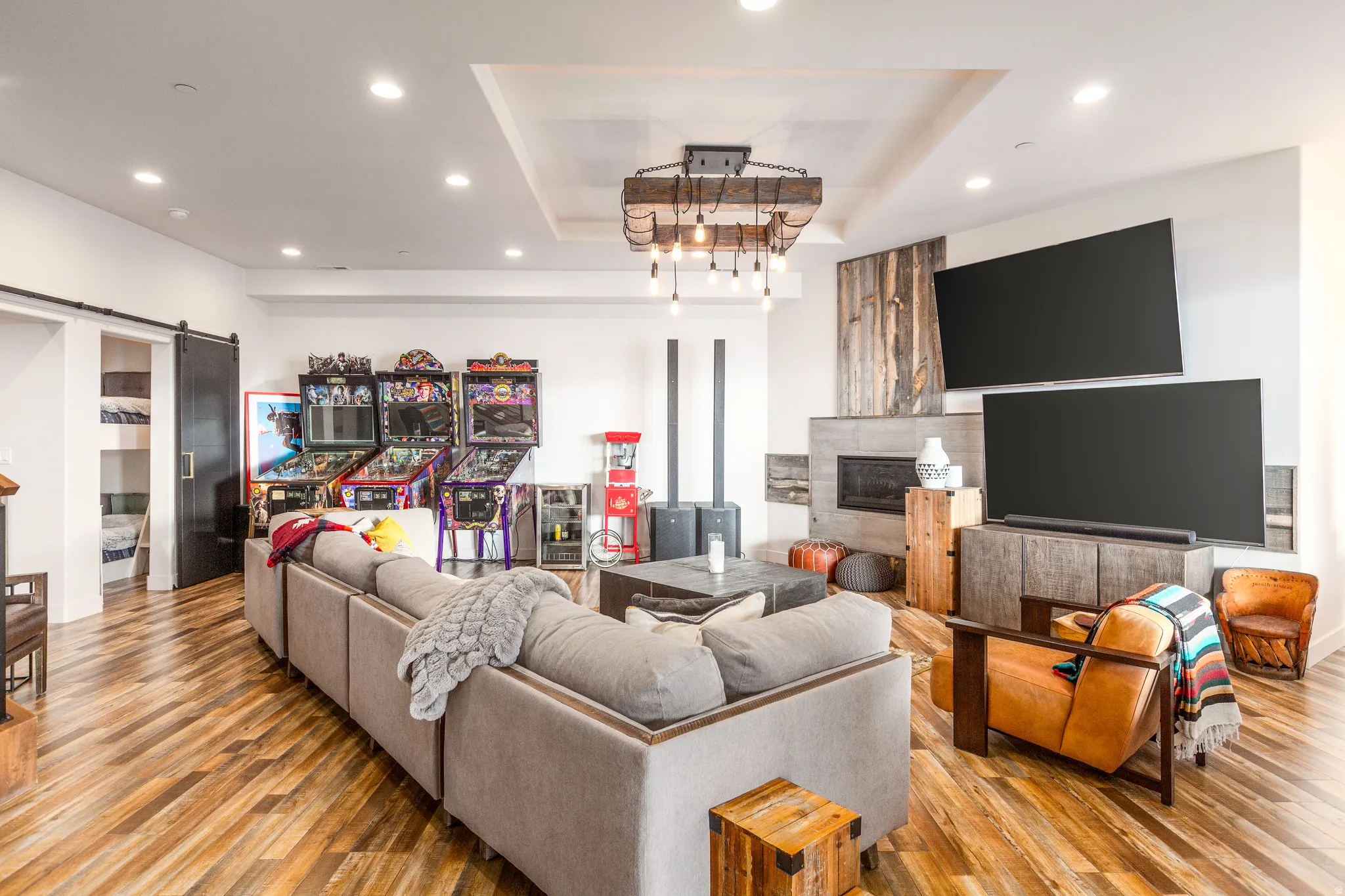 Living room featuring a raised ceiling, recessed lighting, a barn door, wood-type flooring, and a glass covered fireplace