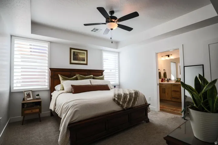 Bedroom with a tray ceiling, carpet flooring, a ceiling fan, and connected bathroom