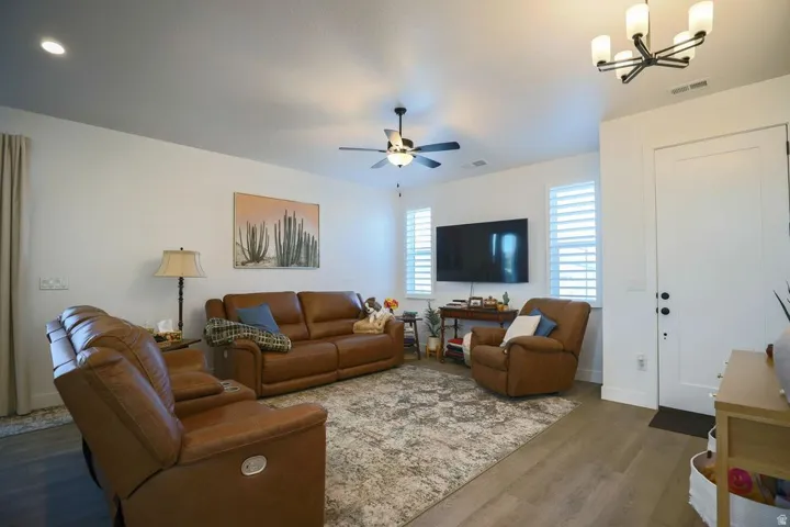 Living area featuring dark wood-style flooring, a ceiling fan, and a chandelier