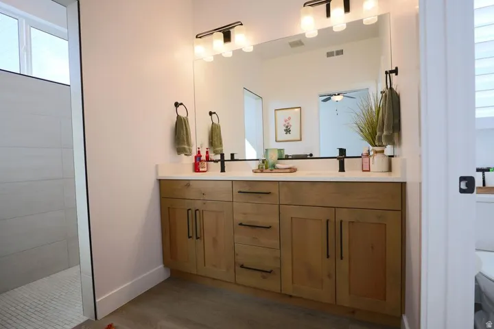 Full bath featuring double vanity and dark wood-type flooring