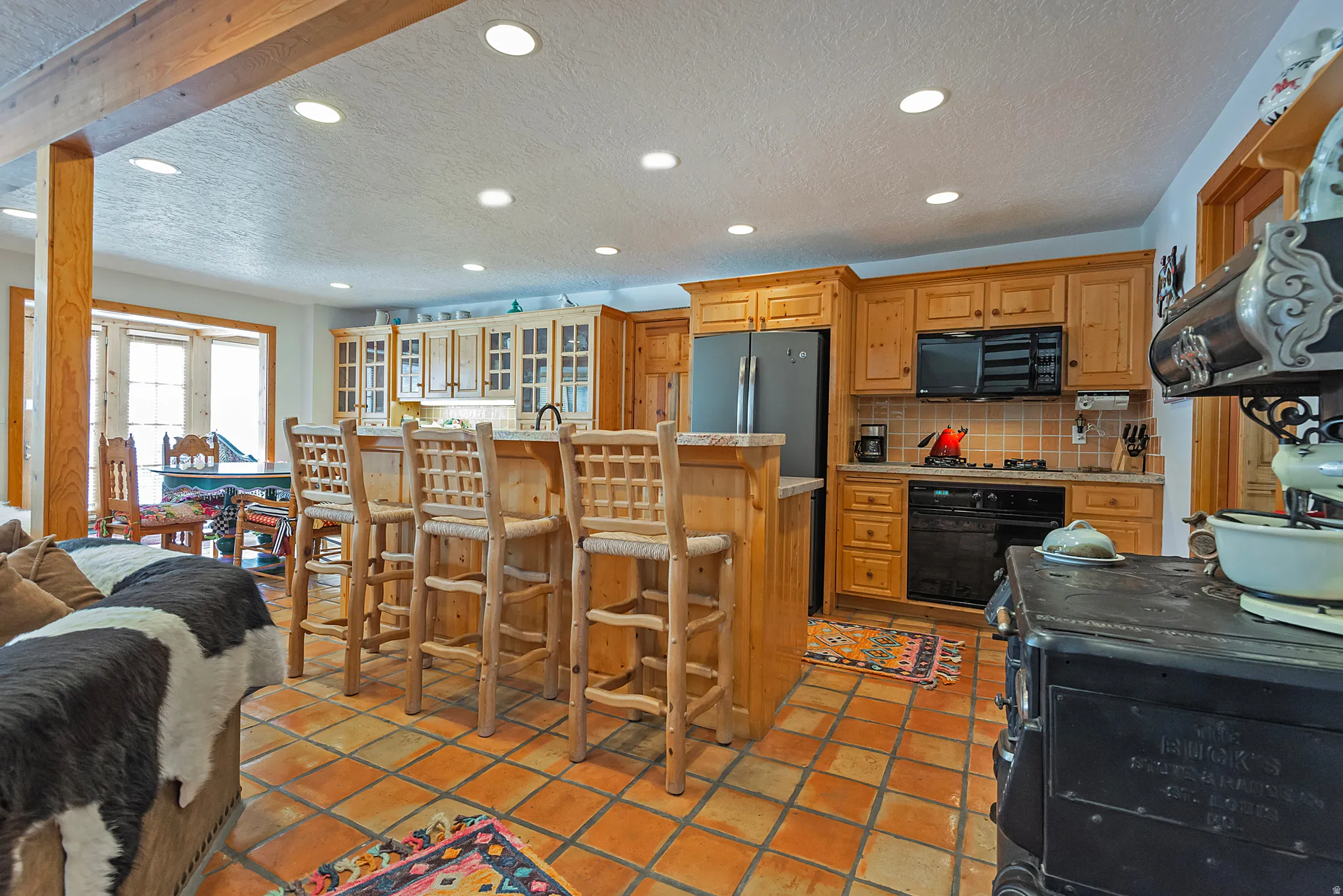 Kitchen featuring a kitchen bar, a textured ceiling, black appliances, an island with sink, and recessed lighting