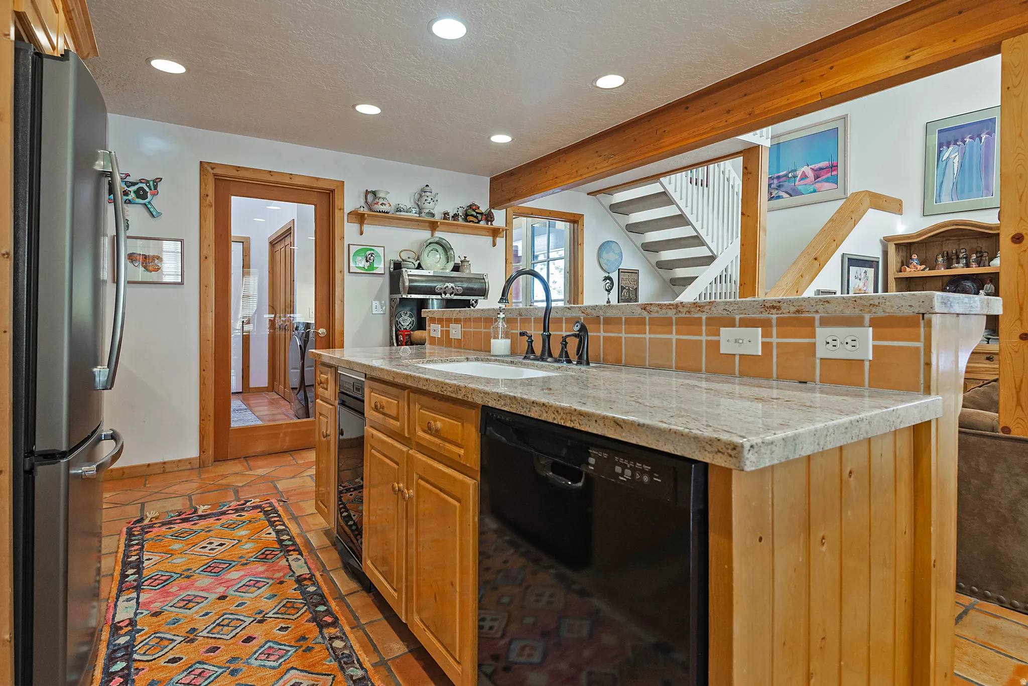 Kitchen featuring an island with sink, dishwasher, freestanding refrigerator, light stone counters, and recessed lighting