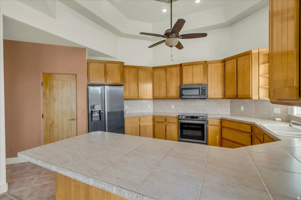 Kitchen featuring open shelves, a high ceiling, appliances with stainless steel finishes, backsplash, and brown cabinetry