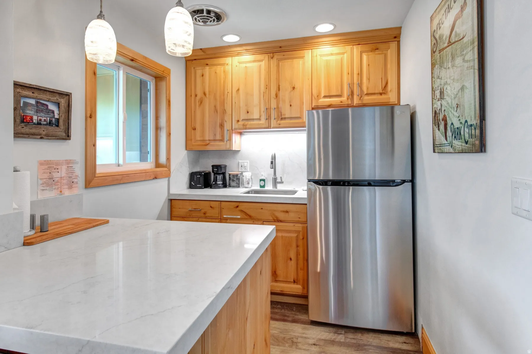 Kitchen featuring freestanding refrigerator, decorative light fixtures, light wood-style flooring, recessed lighting, and light brown cabinetry
