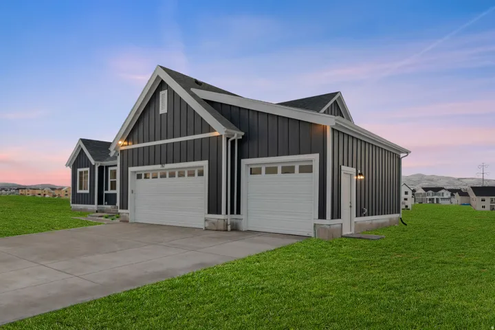 View of front of home with board and batten siding, a lawn, concrete driveway, and an attached garage