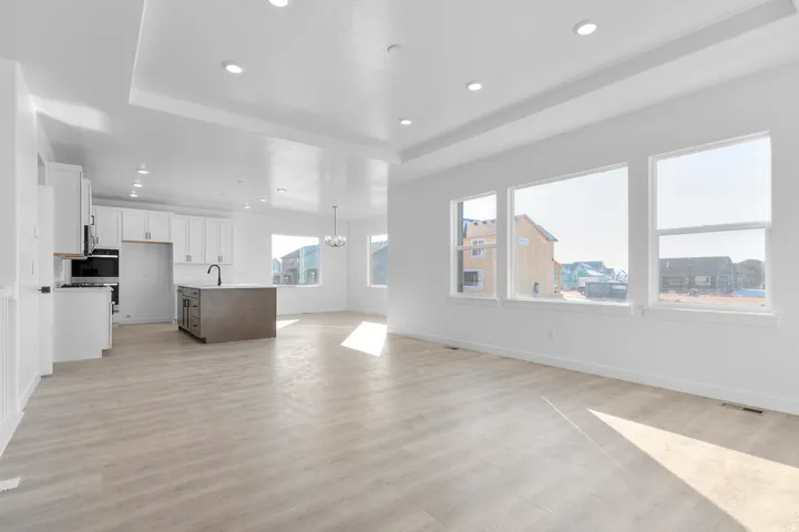 Unfurnished living room with a chandelier, a raised ceiling, light wood-style flooring, and recessed lighting