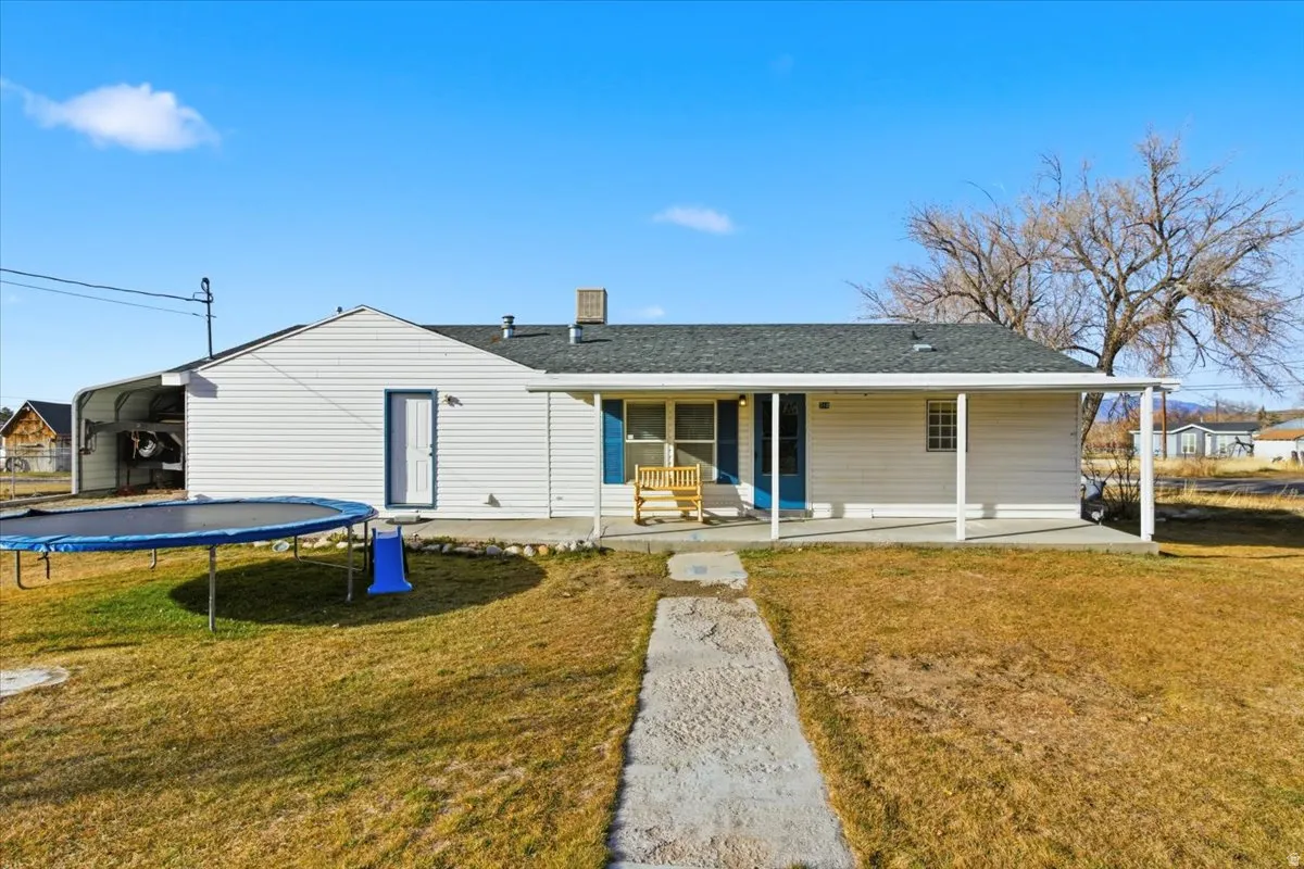 Rear view of house with a trampoline, a yard, covered porch, and roof with shingles