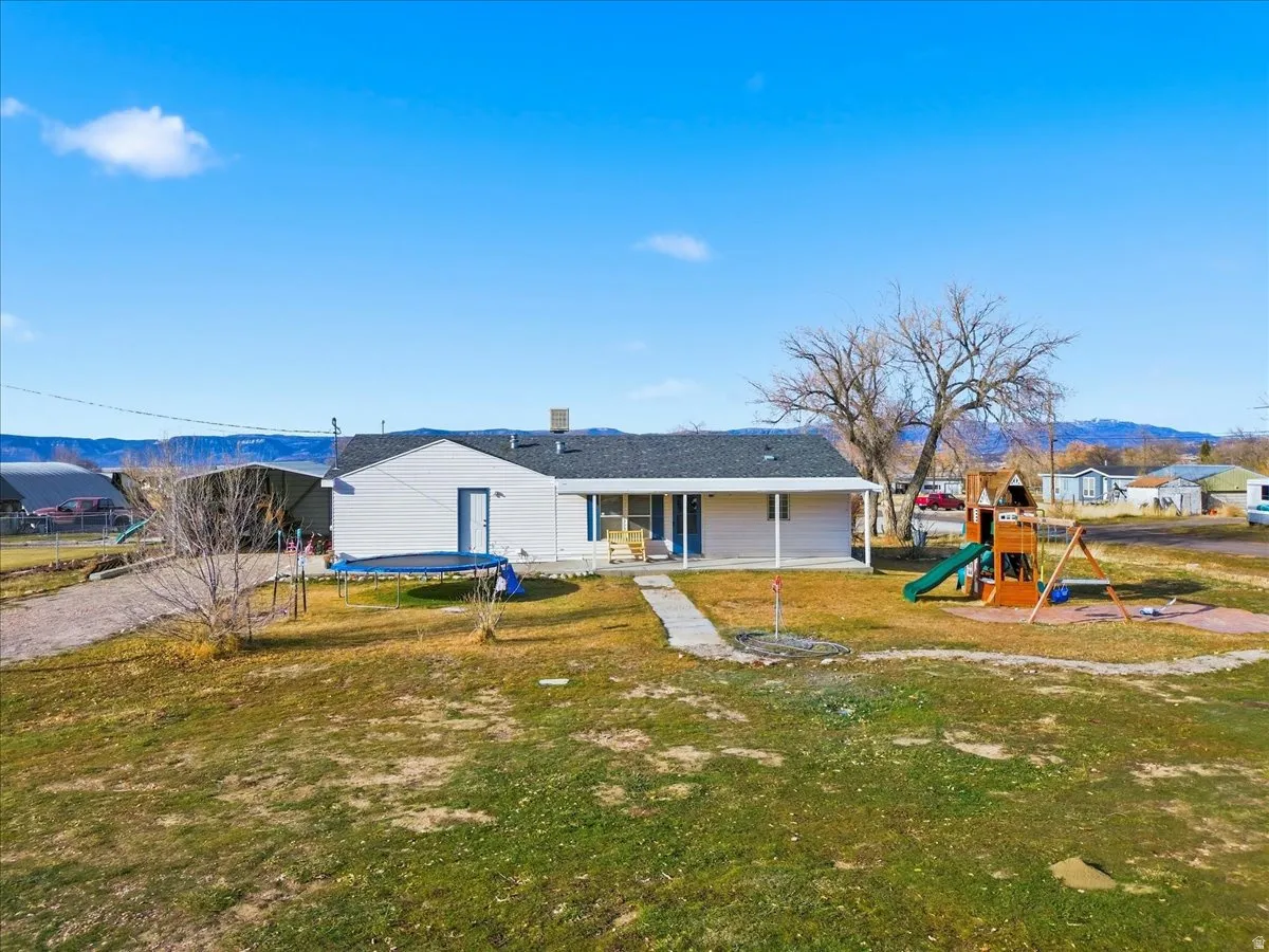 Back of property with a trampoline, a playground, a mountain view, a patio, and a yard