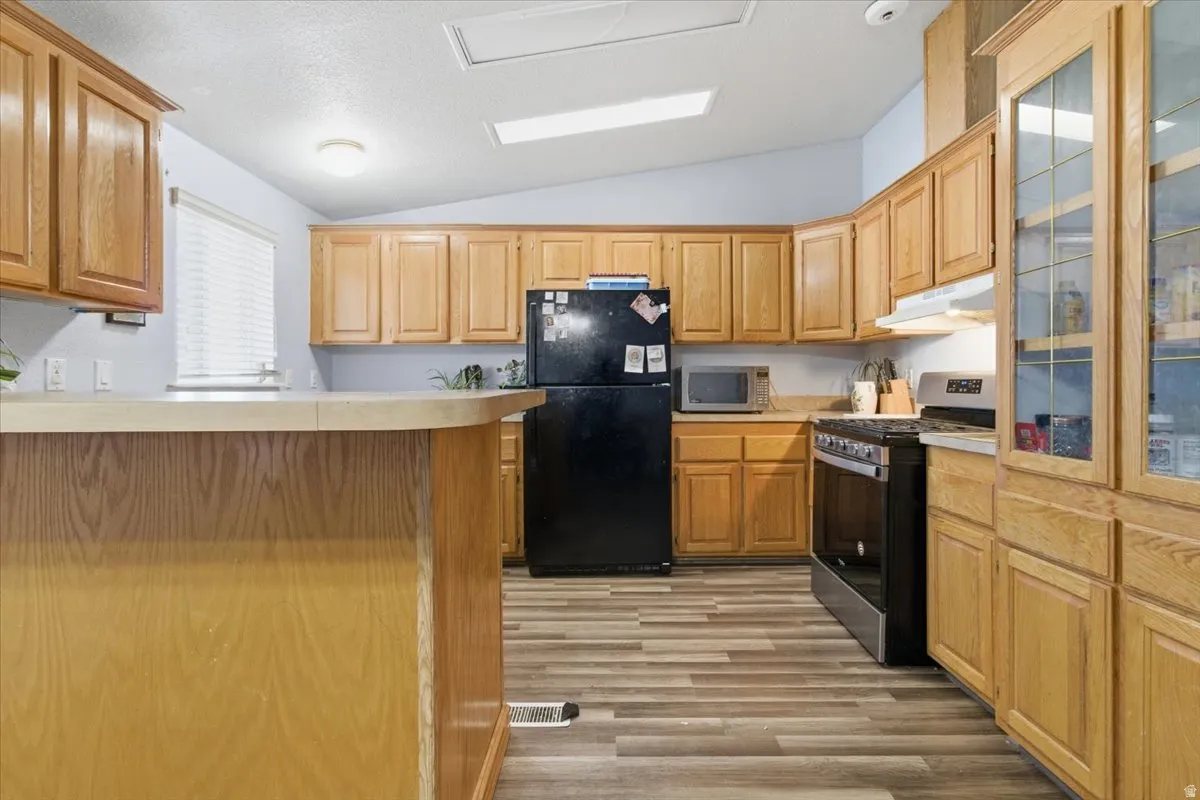 Kitchen featuring lofted ceiling, stainless steel appliances, light countertops, light wood finished floors, and a peninsula