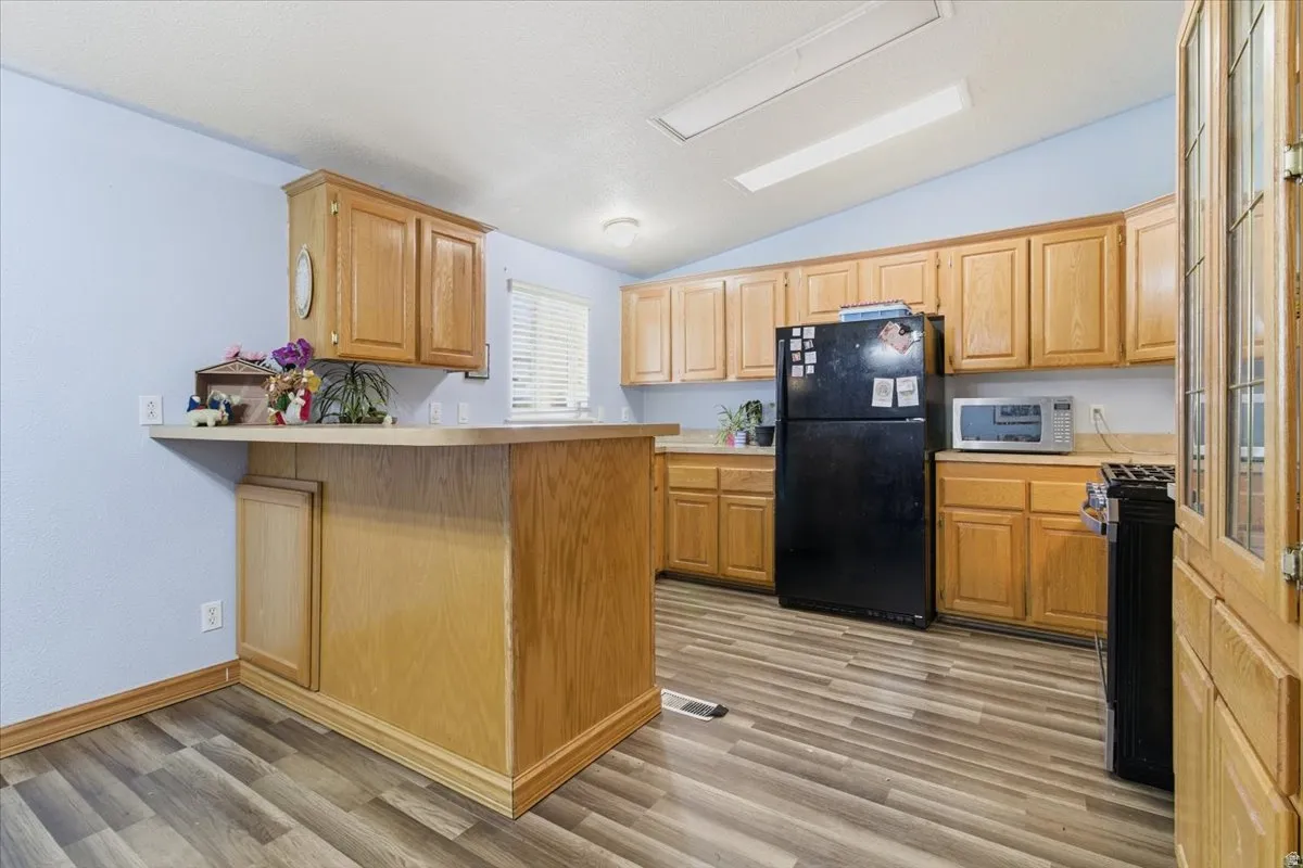 Kitchen with light countertops, a peninsula, lofted ceiling, freestanding refrigerator, and gas stove