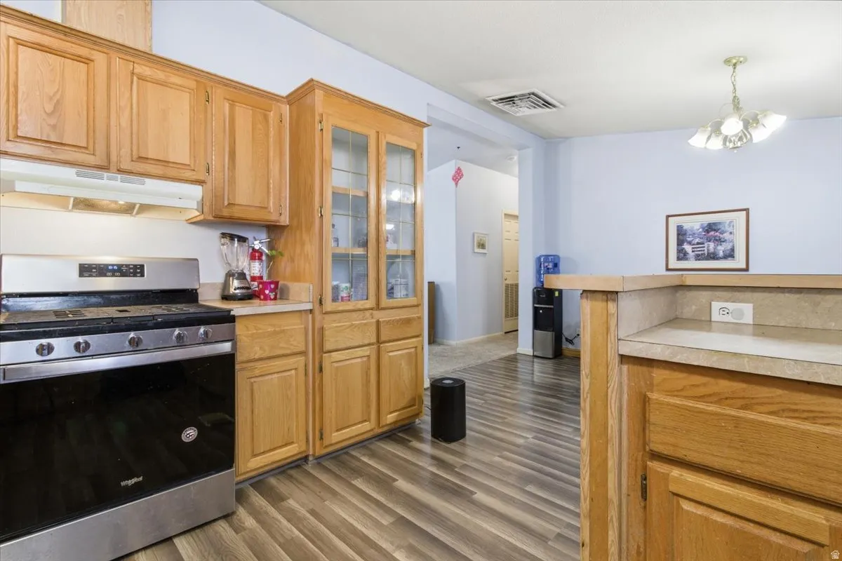 Kitchen featuring gas range, light countertops, under cabinet range hood, and dark wood-style floors