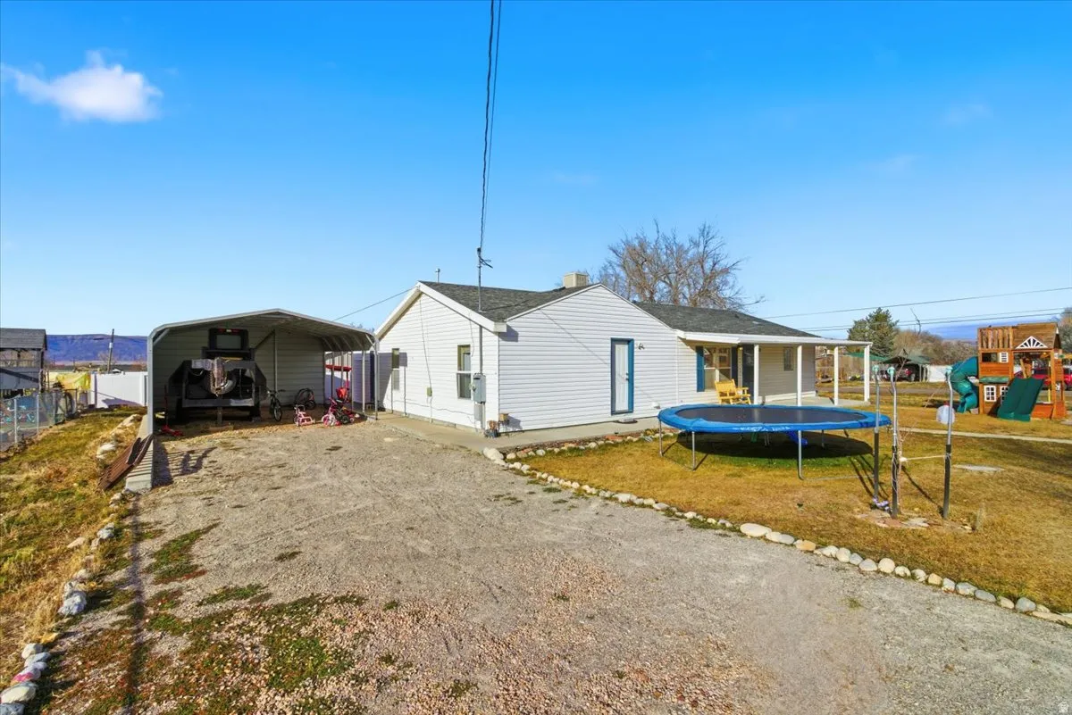 Back of property with a trampoline, driveway, a detached carport, and a lawn