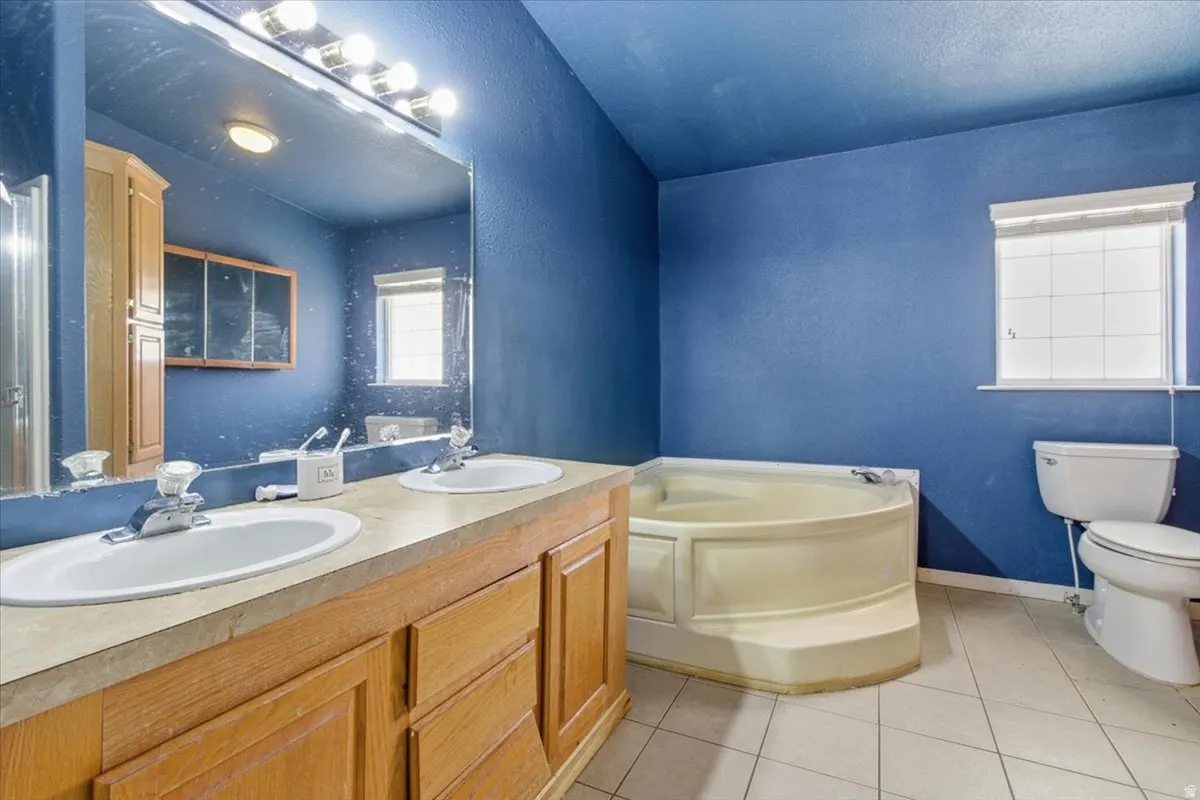 Full bathroom featuring a garden tub, double vanity, light tile patterned floors, and a textured wall