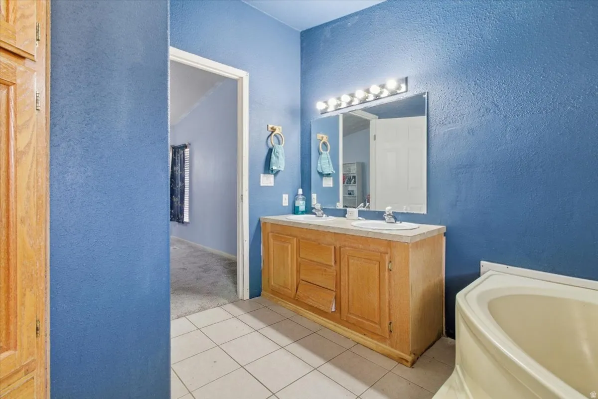 Bathroom with a textured wall, double vanity, a garden tub, and light tile patterned floors
