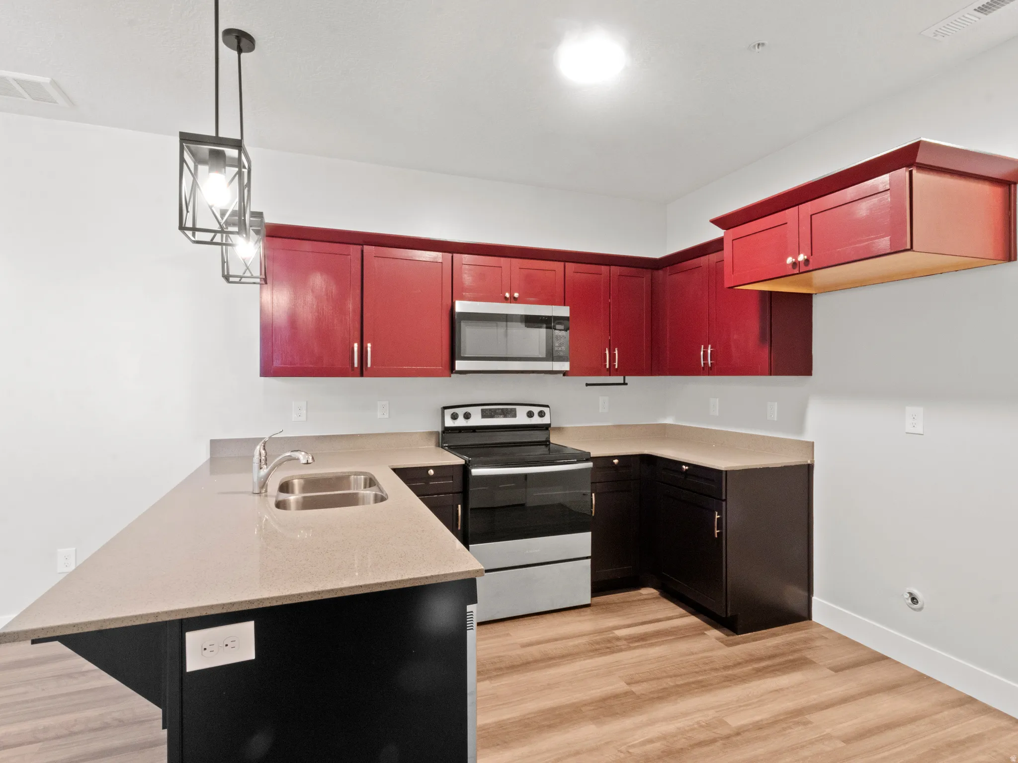 Kitchen featuring stainless steel appliances, decorative light fixtures, a peninsula, light wood-style flooring, and light stone countertops