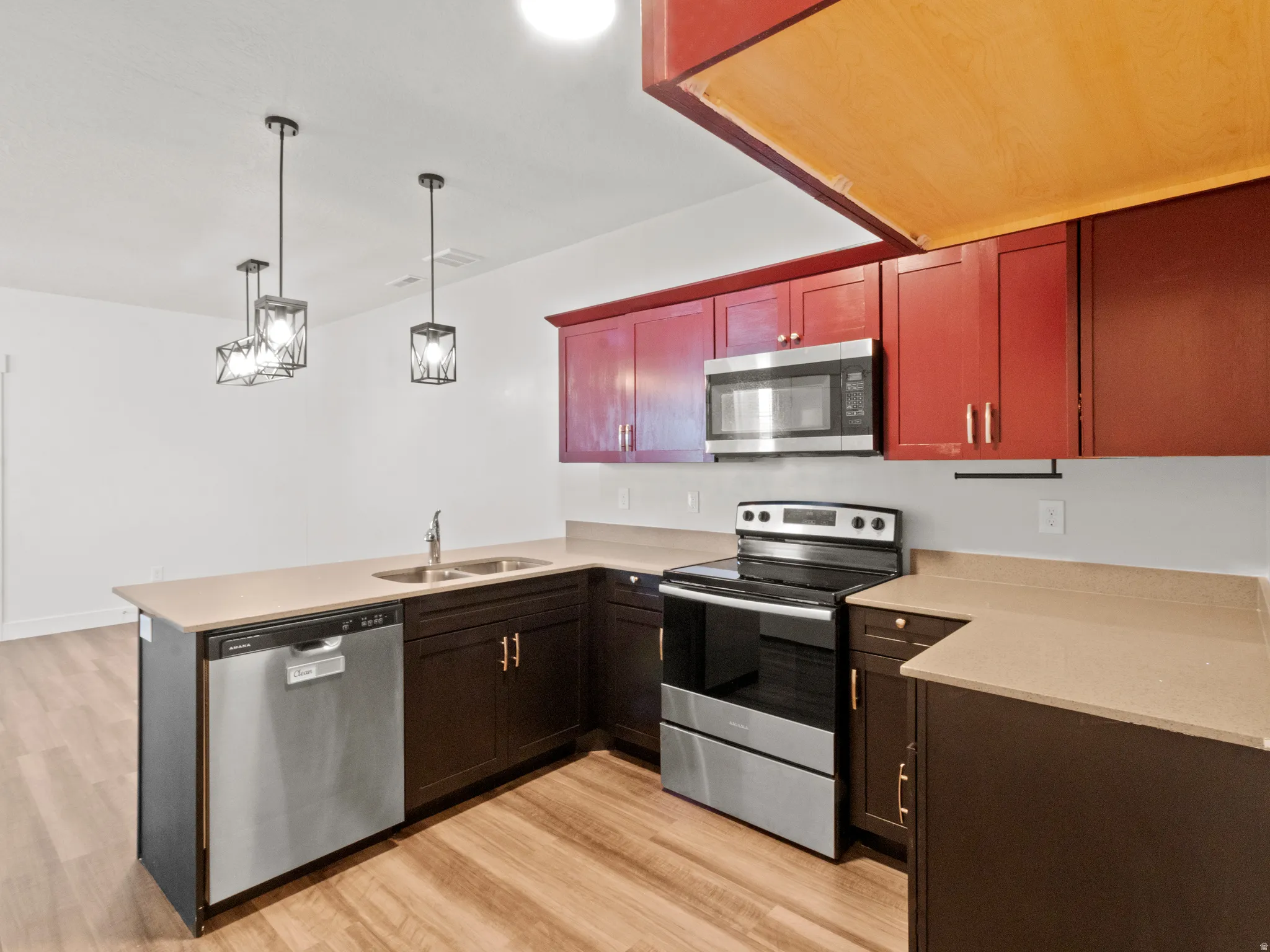 Kitchen featuring appliances with stainless steel finishes, a peninsula, decorative light fixtures, light wood-style floors, and light stone counters