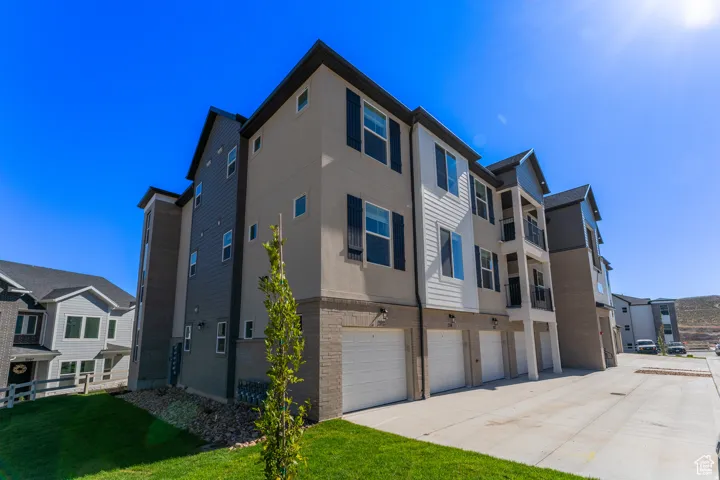 View of property exterior with a garage, driveway, stucco siding, brick siding, and a lawn