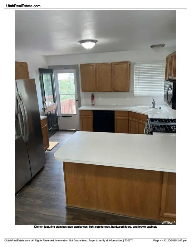 Kitchen with light countertops, brown cabinetry, black appliances, a peninsula, and dark wood finished floors
