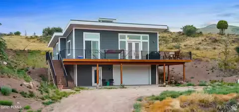 Rear view of property featuring dirt driveway, a wooden deck, a patio, and a garage