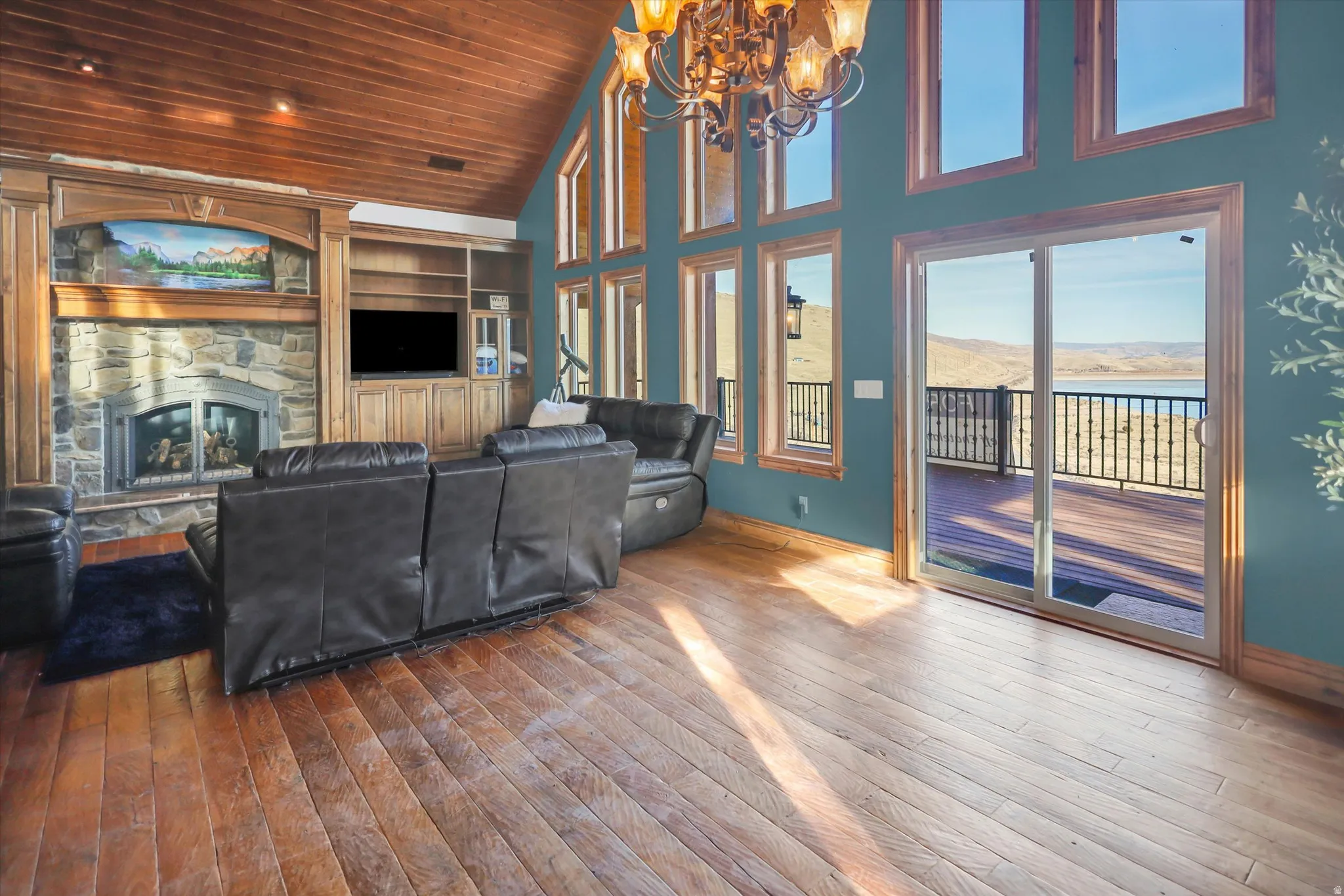 Living area with wood-type flooring, a vaulted wooden ceiling, a stone fireplace, and a chandelier