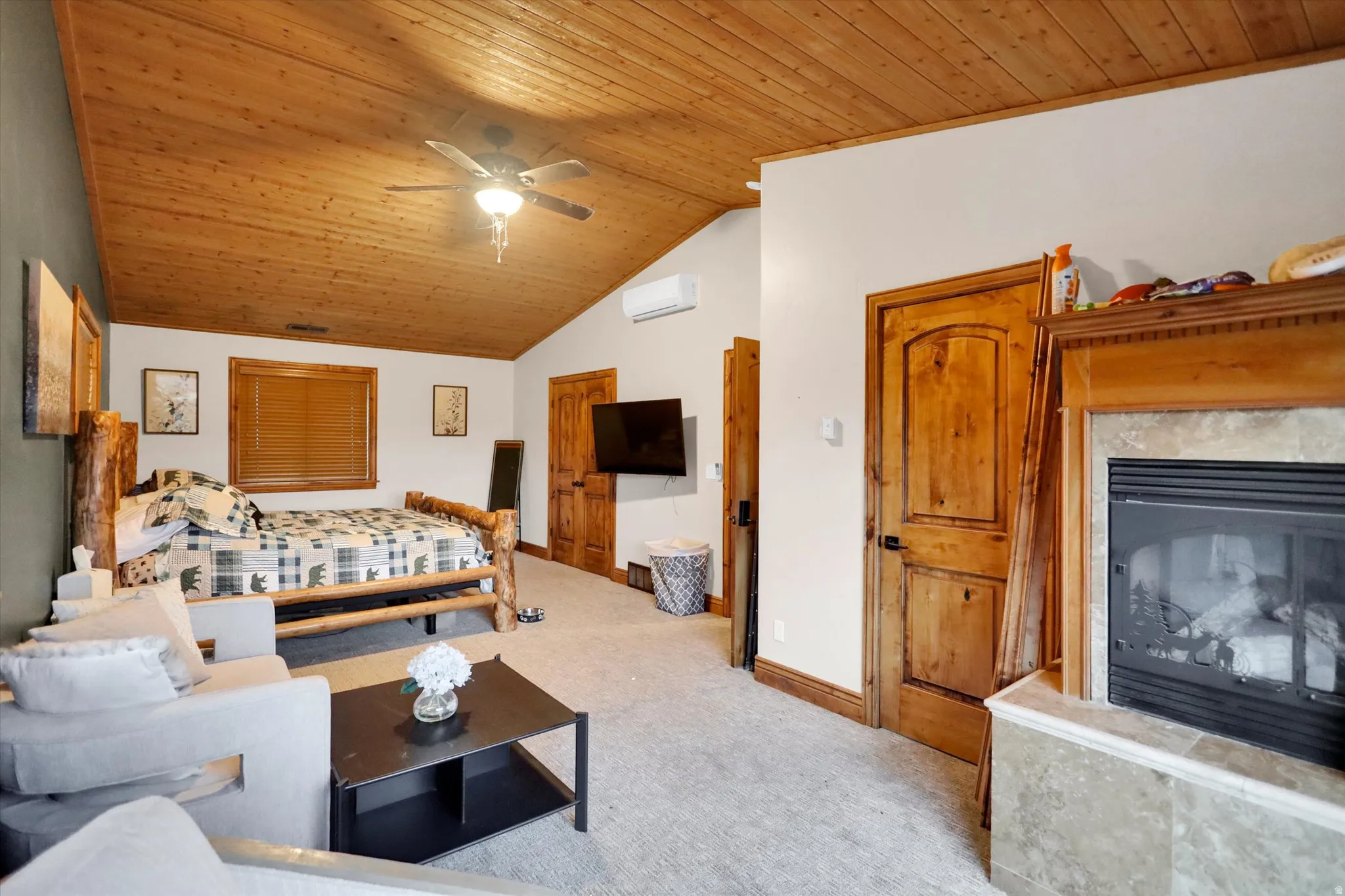 Carpeted bedroom featuring wood ceiling, a high end fireplace, a ceiling fan, lofted ceiling, and an AC wall unit