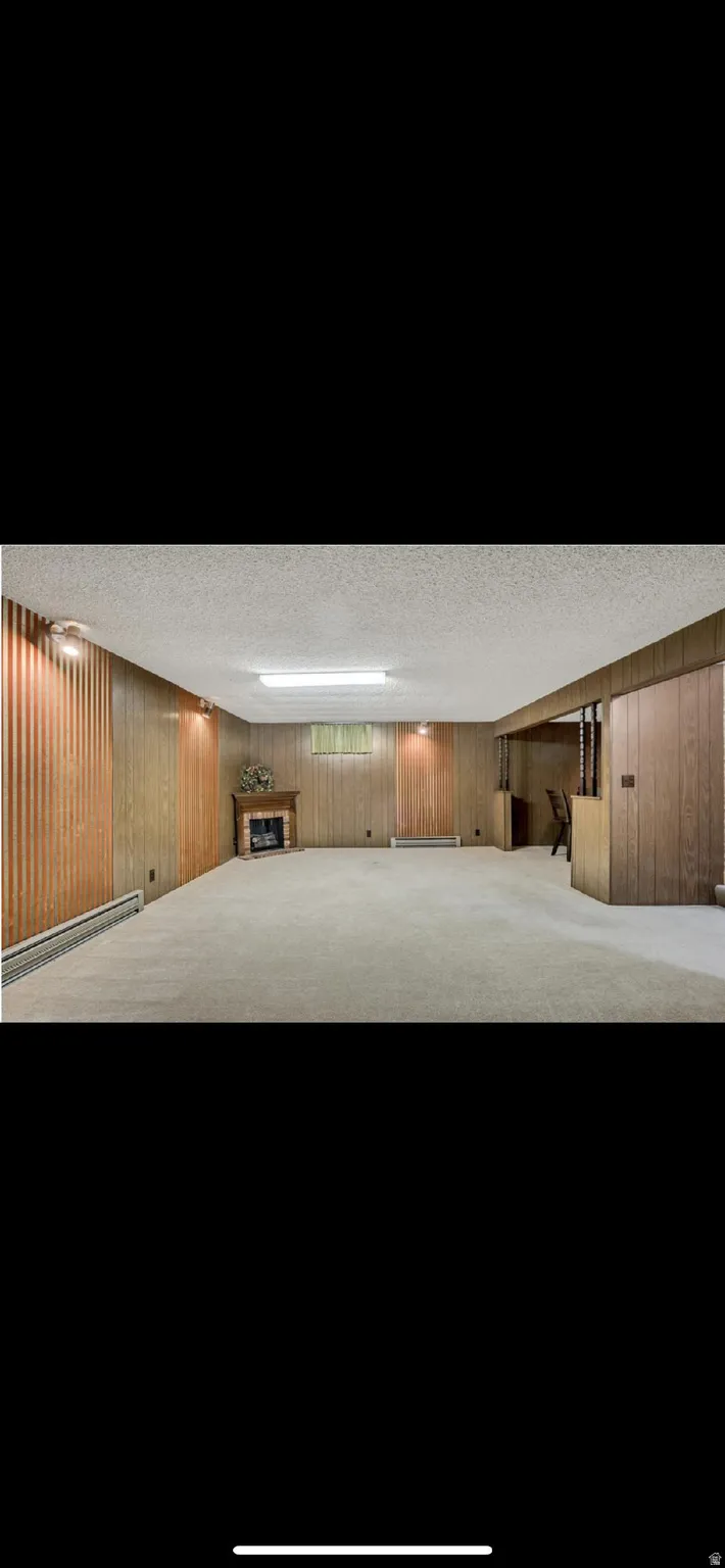 Finished below grade area with wooden walls, a baseboard heating unit, a textured ceiling, and a fireplace