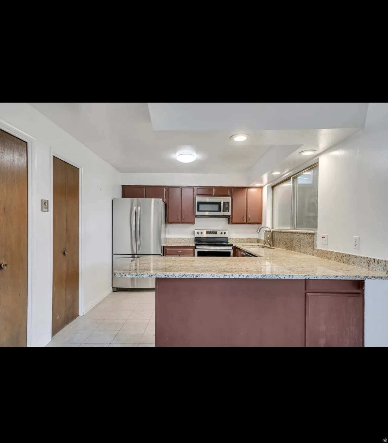 Kitchen featuring appliances with stainless steel finishes, a peninsula, light stone counters, light tile patterned floors, and recessed lighting