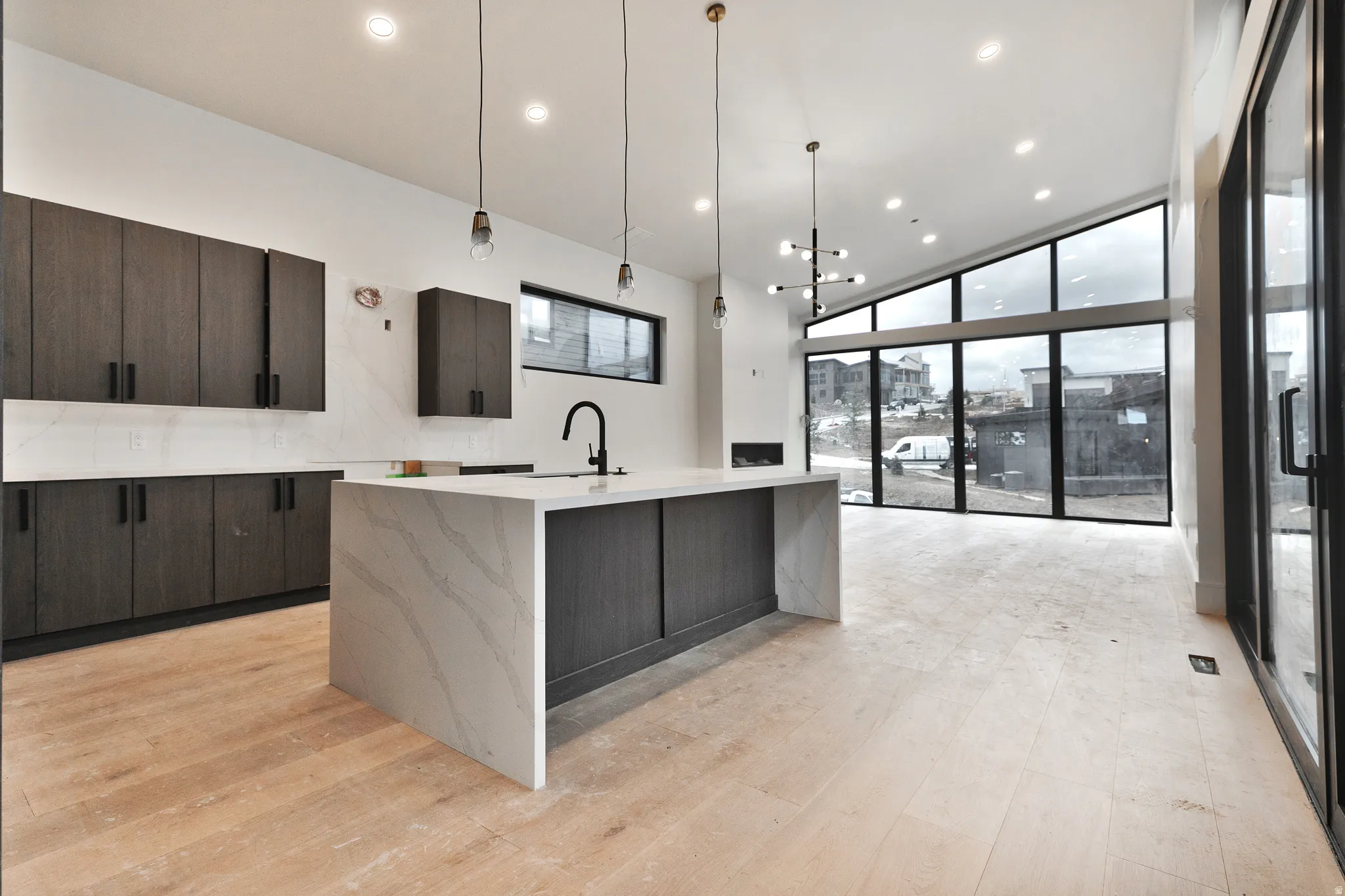 Kitchen featuring modern cabinets, dark brown cabinetry, expansive windows, light stone countertops, and pendant lighting