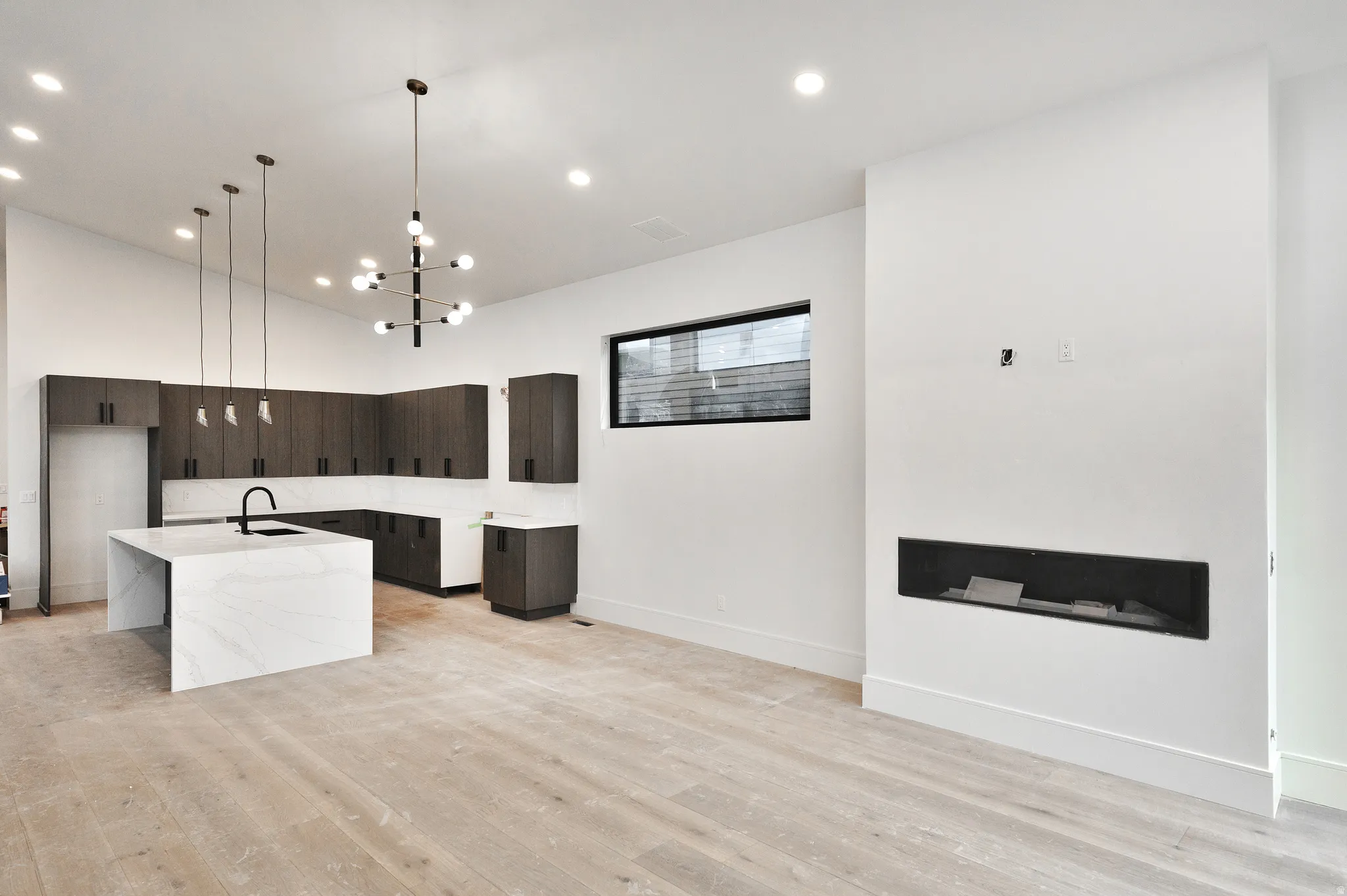 Kitchen with pendant lighting, open floor plan, light wood-style flooring, light stone countertops, waterfall island and modern cabinets