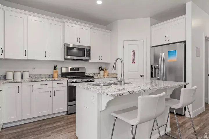 Kitchen featuring stainless steel appliances, a kitchen bar, an island with sink, white cabinetry, and recessed lighting